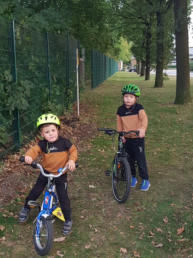Zwei kleine Jungen mit Fahrrädern an einem Zaun. 